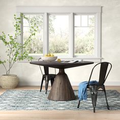 a dining room table with two chairs and an area rug in front of the window