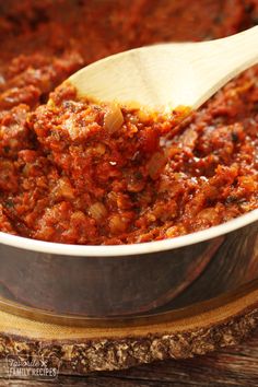 a wooden spoon in a pot filled with chili and meat sauce on top of a cutting board