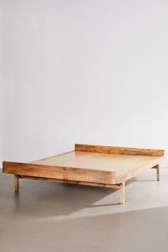 a wooden bed frame sitting on top of a cement floor next to a white wall