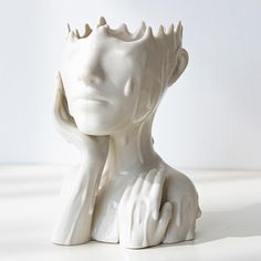 a white ceramic sculpture of a woman's head with hands on her chest