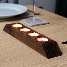 four lit candles are placed in the center of a wooden plank on a table with plates and utensils