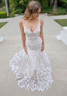 a woman in a white dress is standing on the concrete walkway outside with trees and bushes behind her