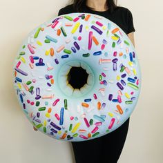 a woman is holding a giant donut pillow with sprinkles on it