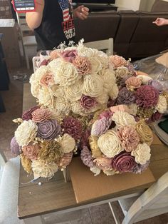 a bouquet of flowers sitting on top of a wooden table next to a person holding a cell phone