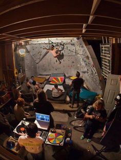 a group of people sitting around in a room with climbing equipment on the wall behind them