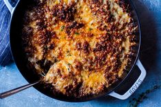 a skillet filled with cheesy cheese and sauce on top of a blue surface