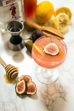 a glass filled with liquid next to sliced figs and honey on a marble counter