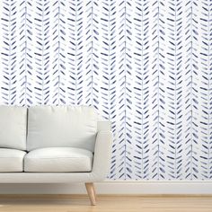 a white couch sitting in front of a wall with blue leaves on it's side