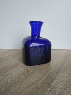 a blue glass vase sitting on top of a wooden table next to a white wall