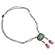 Created just after the turn of the century (circa 1917), this gilt silver jadeite and tourmaline drop necklace was created in China for the export market. Intricately detailed wirework that today would be nearly impossible to create by hand was executed with consummate skill by the early twentieth-century jeweler who created this piece. Even the back is strikingly beautiful. Elaborate wirework balls are stationed along the chain together with white glass beads. The necklace measures 18.5 inches in length. The jade and tourmaline drop hangs an additional 2 ¾ inches. The carved and pierced jadeite jade plaque is a mottled green and the two pink tourmaline drops that are suspended from the jade are without chips are cracks. Minor losses to the wirework topping each tourmaline gem do not mitig Elegant Jade Cabochon Necklace, Vintage Natural Stone Necklace For Formal Occasions, Vintage Natural Stones Necklace For Formal Occasions, Vintage Natural Stone Necklaces For Formal Occasions, Vintage Briolette Necklace For Formal Occasions, Vintage Oval Jade Necklace, Vintage Jade Necklace With Natural Stones, Art Nouveau Gemstone Necklace For Formal Occasions, Vintage Jade Necklace For Formal Occasions