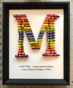 the letter m made out of crayons is displayed in a black frame on a ruler