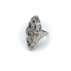 This is part of Chairish’s Fine Jewelry assortment.  This is a stunning Art Deco navette-shaped 18 karat white gold, diamond and sapphire ring. The ring has some excellent filigree work that merges organic abstract shaped with sharp angular lines.   The centre diamond measures 3.35 mm, and the diamonds flanking the centre diamond are 3 mm each, for a total carat weight of approximately .5 carat. The diamonds are three Old European Cuts with high tables. The diamonds are set in octagon shapes. Ab Art Deco 14k White Gold Rings With Gemstone, Art Deco Diamond Ring With Gemstone, Marquise Gemstone Platinum Rings, Marquise Platinum Gemstone Rings, 14k White Gold Marquise Fine Jewelry, Sapphire Diamond Ring With Platinum Accents, Platinum Diamond Ring With Sapphire And Diamond Accents, Platinum Diamond Ring With Sapphire And Accents, Art Deco Oval Sapphire Ring In Platinum