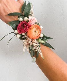 a woman's arm with flowers and greenery attached to it, against a white wall