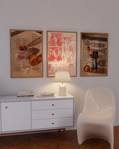 a white chair sitting next to a table with a lamp on it in front of two pictures