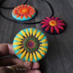 someone is holding three small felt flowers on a table next to a black cord necklace