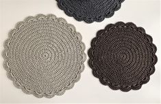 three crocheted placemats are shown on a white table top, one is black and the other is gray