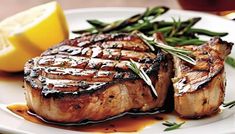 grilled pork chops with green beans and lemon wedges on a white plate