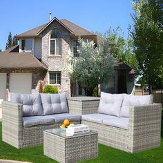 an outdoor furniture set in front of a house with grass and flowers on the lawn