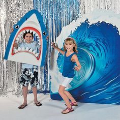 two children are standing in front of a backdrop with a shark and a man holding a surfboard