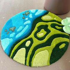 a green and blue rug on the floor next to a potted plant with flowers