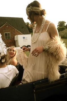 a woman in an old fashion dress and feathered headdress is talking to two other women