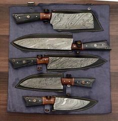 five knives are lined up in a row on top of a blue cloth with brown leather handles