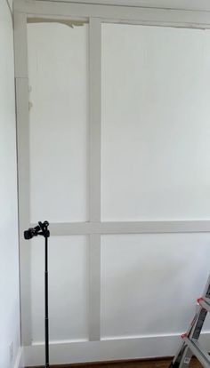 a ladder leaning against a white wall next to a window with no curtains on it