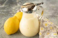 two lemons are next to a pitcher of milk and a cloth on the table