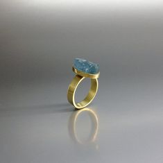 The sides of this raw stone ring are polished to secure a firm hold and give a the opportunity to cut a geometrical shape. It is set in 18K gold with a 4mm / 0.15inches band and a small rim embracing the stone. The stone is of high quality and stunns with its beautiful color. All our stones are natural stones and our jewelry is handmade, very slight differences may occur in color and size. Size stone: 14x8x8mm Aquamarine: The Romans believed it was sacred to Neptune and was a gift by the sirens, Modern Gold Rings With Blue Topaz, Modern Aquamarine Oval Rings, Modern Oval Aquamarine Rings, Yellow Gold Aquamarine Ring As Gift, Yellow Gold Aquamarine Rings For Gifts, Modern Oval Blue Topaz Ring, Modern Topaz Birthstone Ring As Gift, Modern Topaz Ring As Birthstone Gift, Unique Aquamarine Oval Rings