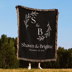 a black and white wedding banner hanging from the side of a field with trees in the background