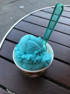 a bowl filled with blue ice cream sitting on top of a wooden table next to a green spoon