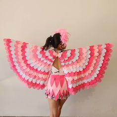 a woman in a pink and white costume with large wings on her back, standing next to a wall