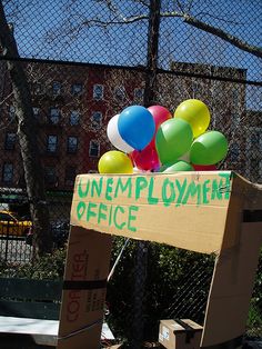 a cardboard box with balloons in it sitting on the ground next to a fence and building