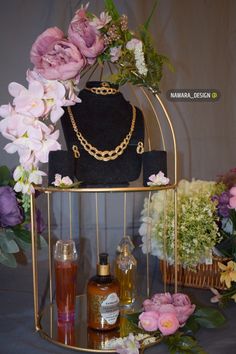 a gold jewelry stand with flowers and bottles on it's display shelf, next to a mannequin wearing a necklace