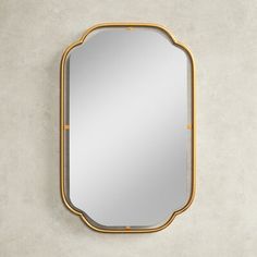 a gold framed mirror on the wall with a concrete surface and white walls in the background