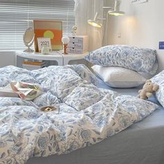 an unmade bed with blue and white bedspread, pillows and a teddy bear