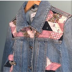 a denim jacket with patchwork on the back and pink linings, hanging from a wooden hanger