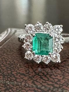 Bright vintage emerald and diamond cluster ring in 18k white gold. Set with an octagonal step cut emerald of 1.11 carats in a square cluster of twelve round brilliant cut diamonds all totaling 0.92 carats. Beautiful deep green emerald with natural inclusions. The square border of brilliant cut diamonds frame it with lively sparkle. British hallmarks including makers mark PD and 18K. Assay office mark a little unclear, and date letter W probable for 1964. Nice finger coverage at 1/2 inch tall. To Square Border, Antique Ring Box, White Gold Set, Letter W, Step Cut, Diamond Cluster Ring, Green Emerald, Multi Stone Ring, Diamond Cluster