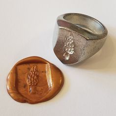 a silver ring sitting next to a wax stamp on a white surface with a piece of fruit in the middle