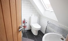 a white toilet sitting under a window next to a sink and radiator in a bathroom