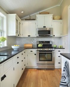 a kitchen with white cabinets, black counter tops and wooden floors is pictured in this image