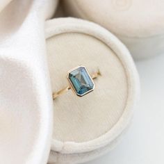 an engagement ring with a blue topazte sits on a white cloth covered box