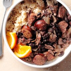 a white bowl filled with rice, meat and orange wedges next to a fork