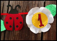 paper flowers and ladybug decorations on a wooden table with the number one pinned to them