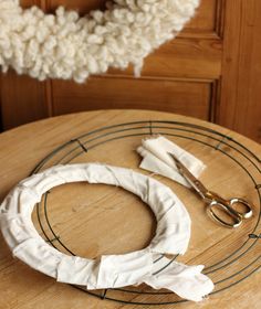 a pair of scissors sitting on top of a wooden table next to a white wreath