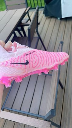 a person holding a pink nike shoe on top of a wooden deck next to a picnic table