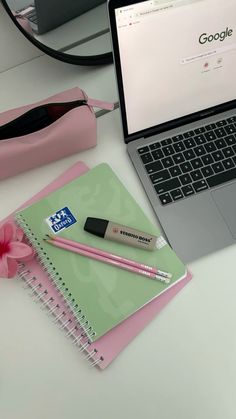 an open laptop computer sitting on top of a white desk next to a pink flower