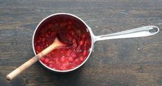 a wooden spoon in a pot filled with raspberry sauce on top of a table