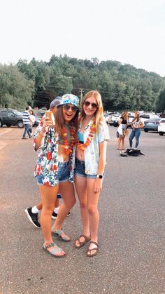 two young women standing next to each other in a parking lot with cars behind them