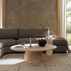 a living room with a couch, coffee table and vase on the floor in front of a large window